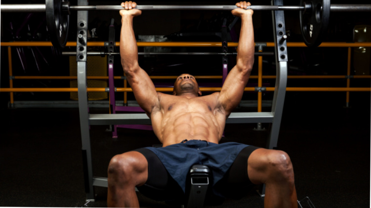 A muscular person on a bench press lifting a barbell on an incline bench.