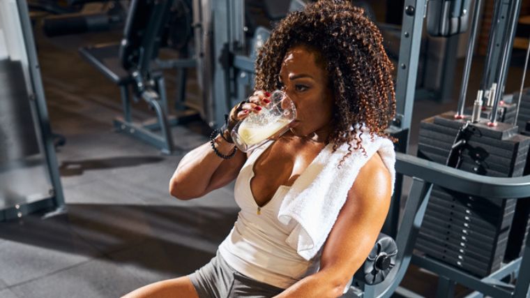 A gymgoer drinking whey powder shake from a glass.