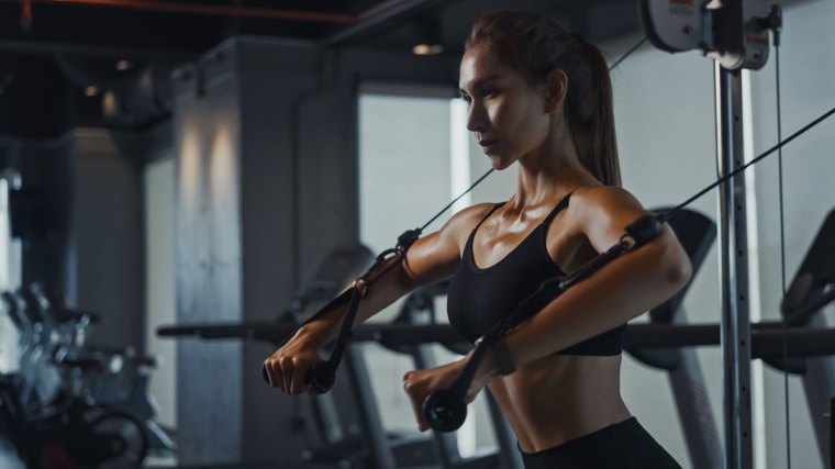 A fit person working out in the gym with a cable machine.