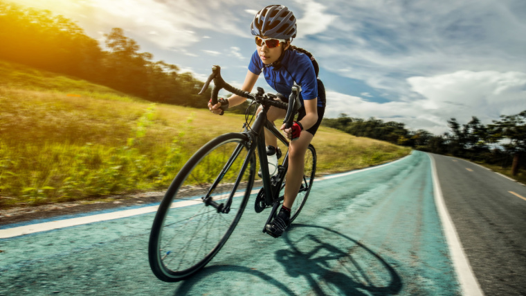 A person cycling outdoors and leaning forward on their bicycle.