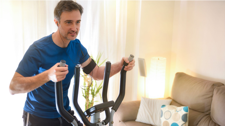 Smiling man doing elliptical bike sport in the living room.