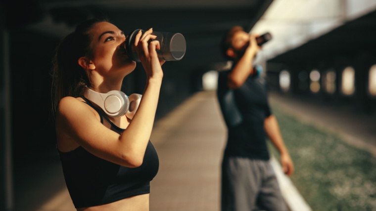 Two fit people drinking a protein shake.