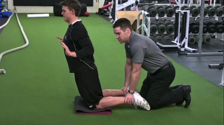 A coach helping someone do the Nordic curl.