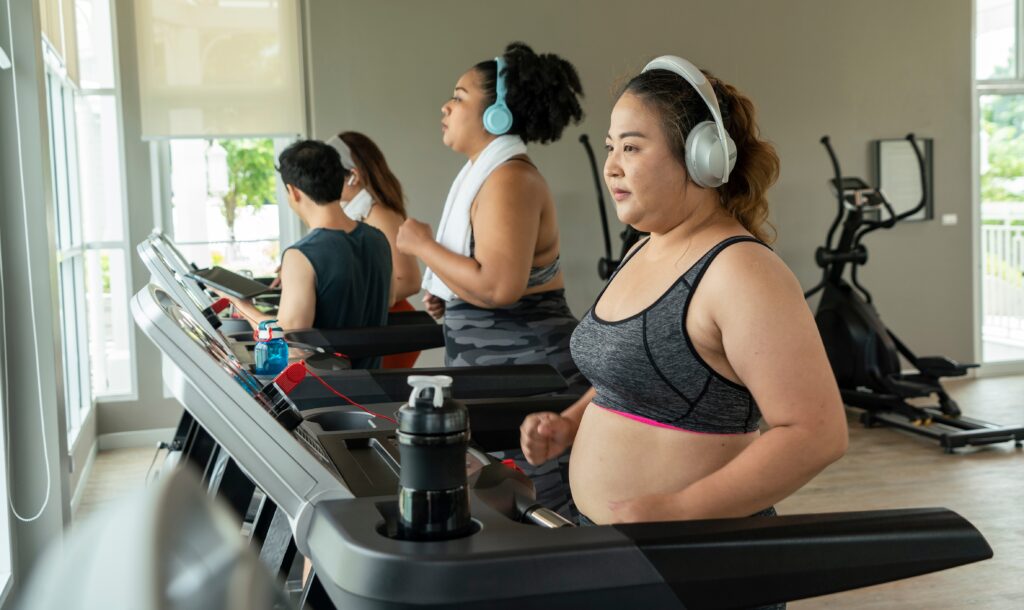 Three women and one man walking on treadmills in a gym.