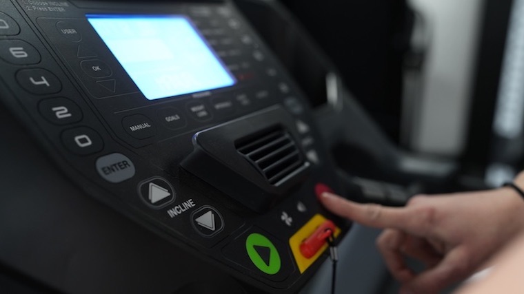 A hand pushes the stop button on a Schwinn 810 Treadmill control panel