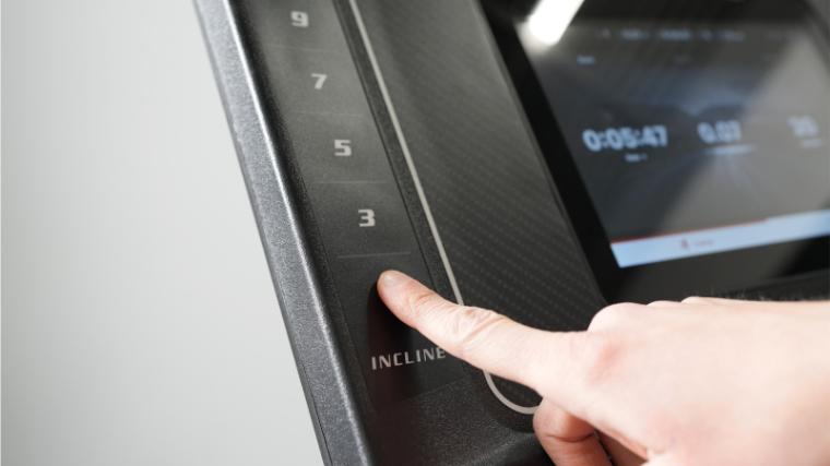 A hand reaches out to adjust the incline on the Sole F80 treadmill.